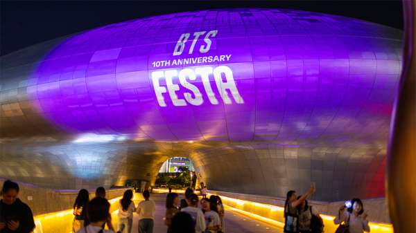 People gather to celebrate the tenth anniversary of BTS at the Dongdaemun Plaza in Seoul, South Korea. Fans are taking pictures with a landmark building covered in purple, with a sign that reads