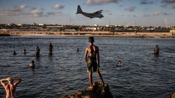 سباحون ينظرون إلى طائرة عسكرية تهبط في قاعدة جوية في العاصمة الصومالية مقديشو يوم الجمعة.