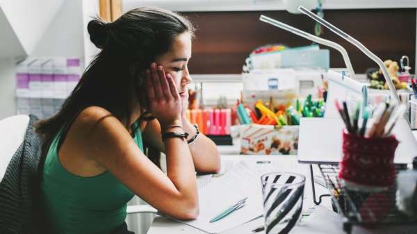 A young woman sits at a desk looking sad with her head in her hands