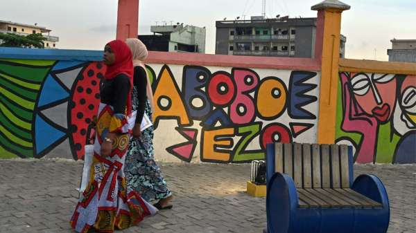 امرأتان تسيران بجانب حائط مغطى بالغرافيتي في حي أبوبو في أبيدجان، عاصمة ساحل العاج الجمعة.