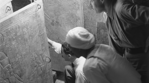 هوارد كارتر ومساعده آرثر كالندر ورجل مصري مجهول الهوية يفتحون أبواب مزار مذهّب داخل مقبرة توت عنخ آمون